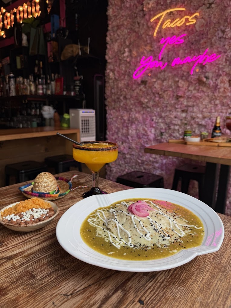 Enchiladas verdes with a mango margarita under a pink neon sign