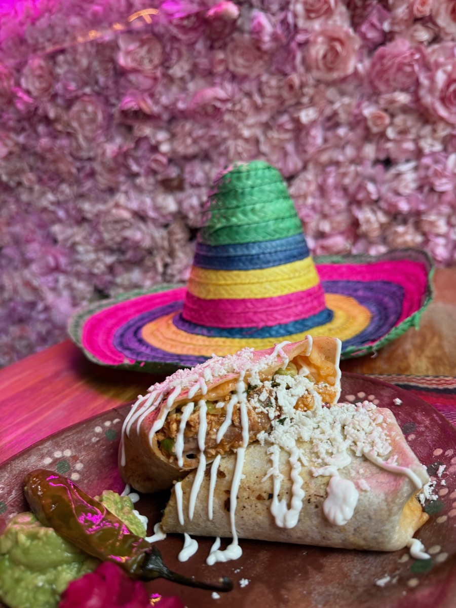 Two burritos drizzled with crema on a terracotta plate beside a mini sombrero