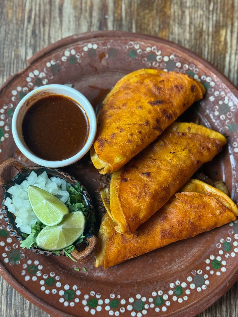 Three quesabirria tacos on clay plate with consomé for dipping