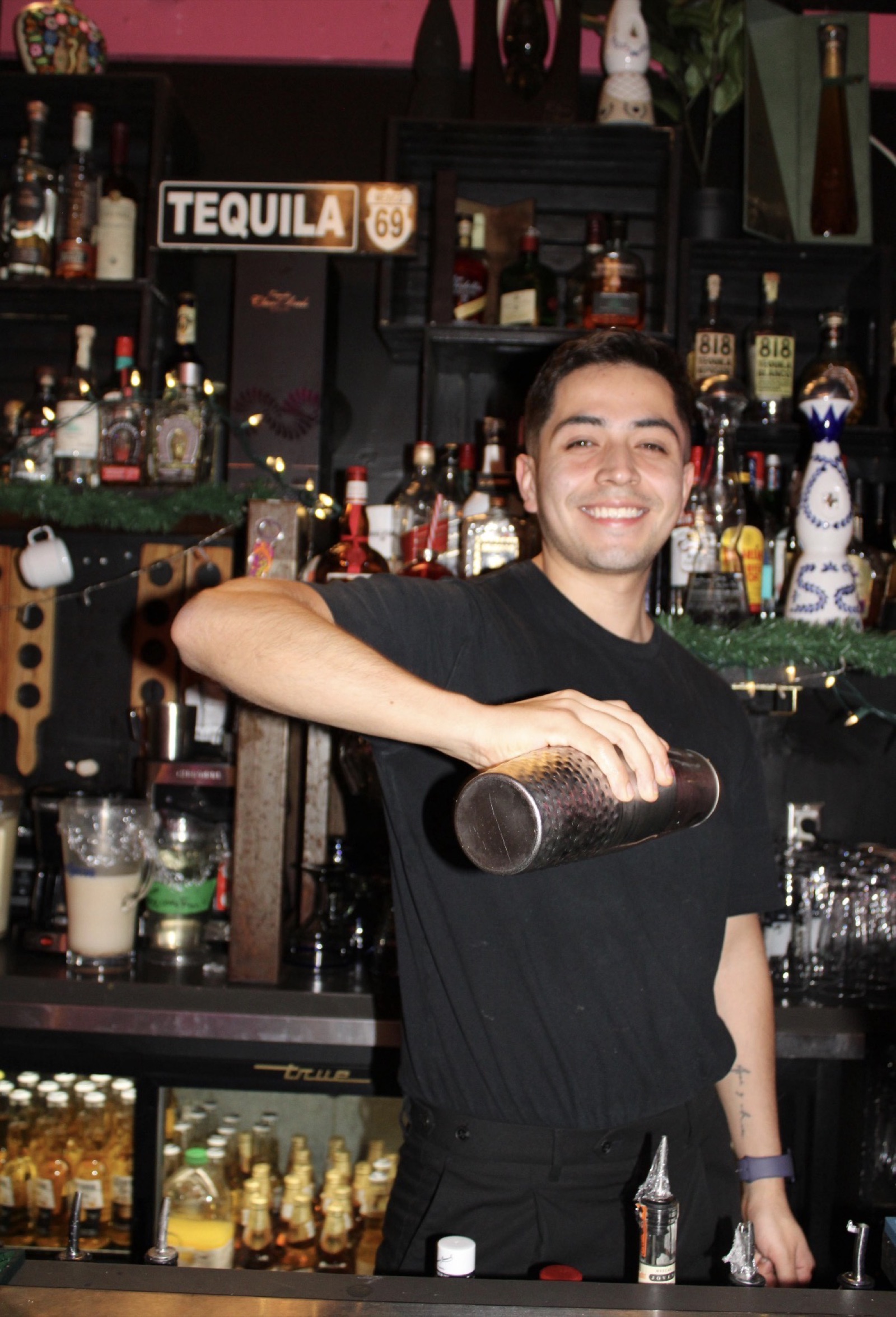 Bartender mid-shake at the bar with the spirits wall behind