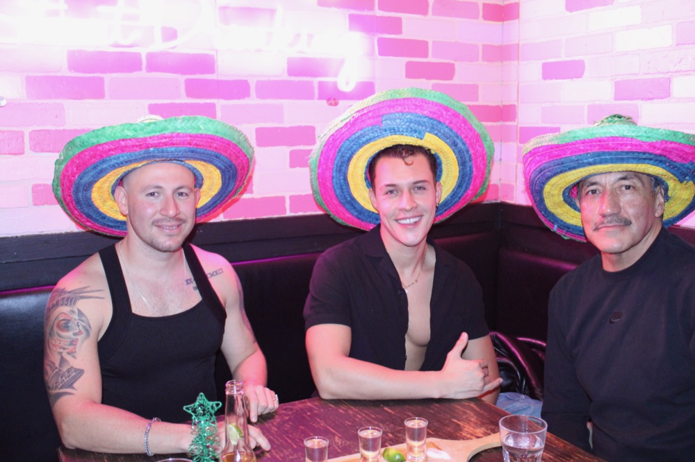 Three friends in sombreros sharing tequila shots at the bar