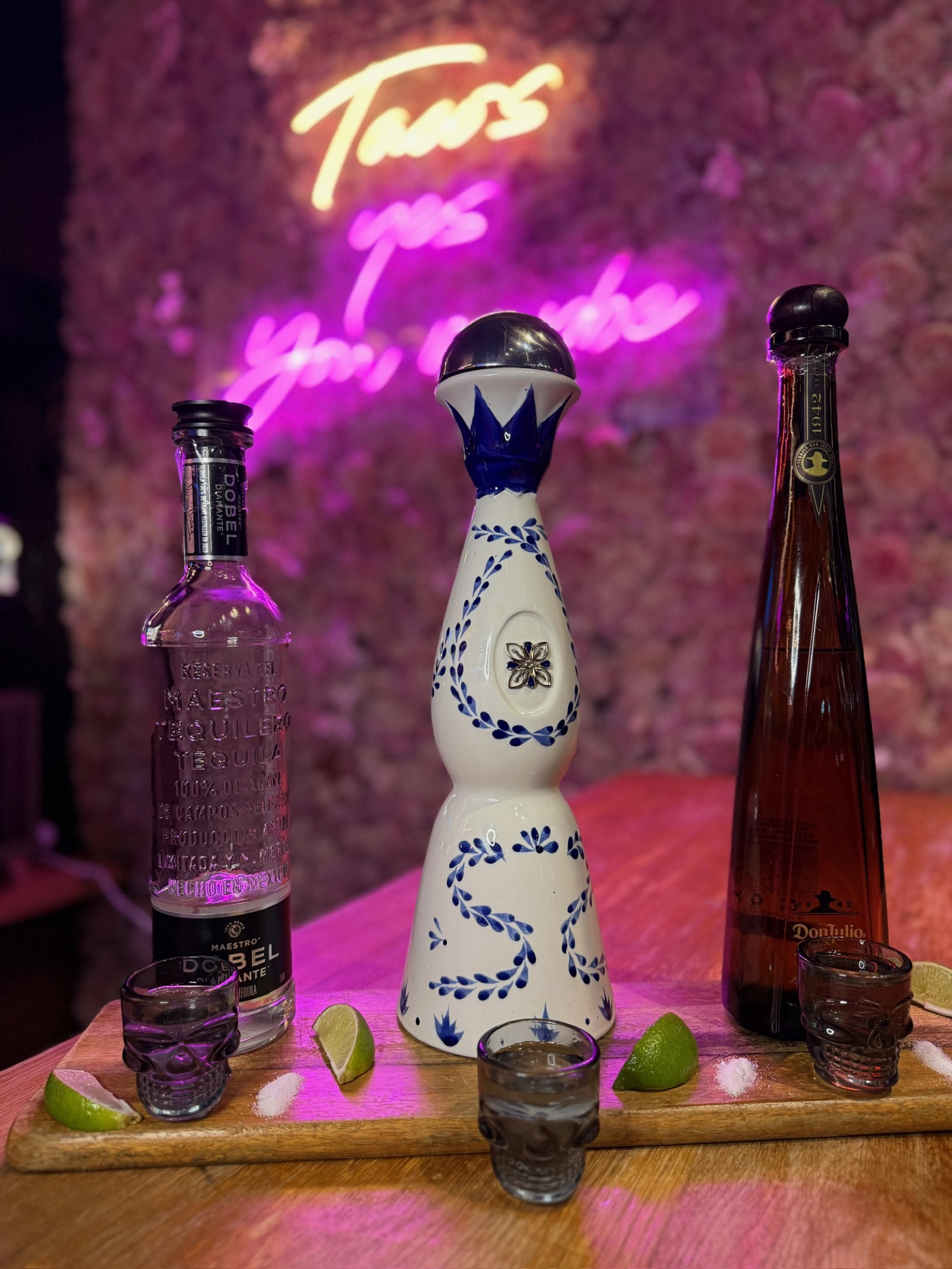 Premium tequila bottles and skull shot glasses with limes under the neon sign